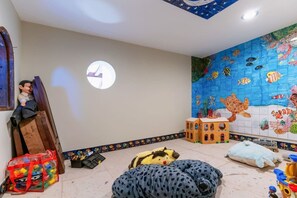 A child's playroom with an ocean-themed wall mural, a round ceiling light, and various toys.