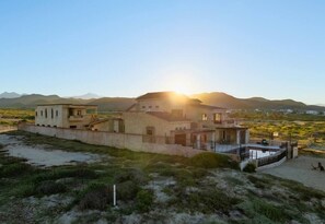 A coastal property with a large house, a swimming pool, and a view of the sea and mountains.