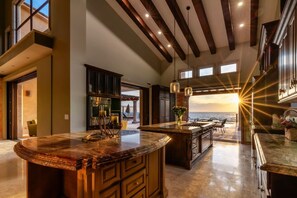 A spacious kitchen with a large island, dark wood cabinetry, and a view of the ocean. - Château Cerritos | Luxe Oceanfront Home (La Paz)