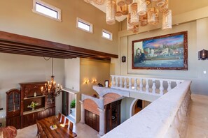 A spacious dining area with a high ceiling, a chandelier, and a view of the outdoors. - Château Cerritos | Luxe Oceanfront Home (La Paz)