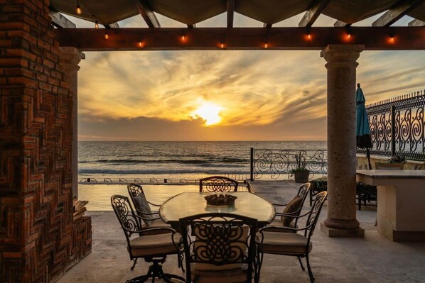 A terrace with a table and chairs, overlooking the ocean at sunset.
