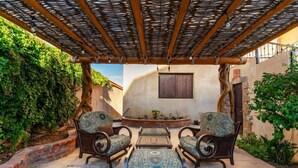 Een terras buiten met rieten meubilair, een bakstenen muur en een houten pergola.