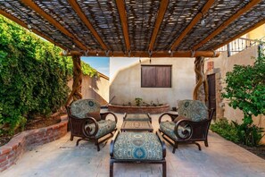 An outdoor patio with wicker furniture, a brick wall, and a wooden pergola. - Château Cerritos | Luxe Oceanfront Home (La Paz)