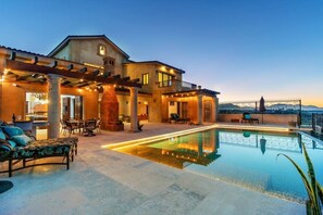 Una casa de dos pisos con piscina, mobiliario exterior y vistas a las montañas.