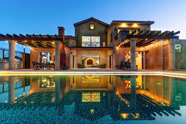 Una casa lujosa con piscina, mobiliario de exterior e ingreso bien iluminado.