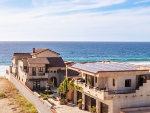 Una propiedad costera con una casa amplia que tiene un balcón, techo con paneles solares y vista al mar.