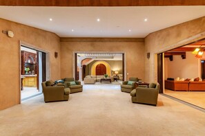 A spacious lobby with a central seating area, a kitchen visible through an open door, and a separate seating area with a sofa and lamp. - Château Cerritos | Luxe Oceanfront Estate (La Paz)