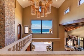 A spacious interior with a balcony overlooking a beach, a large window, and a staircase. - Château Cerritos | Luxe Oceanfront Estate (La Paz)