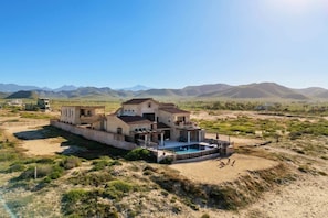 A large house with a swimming pool, surrounded by a desert landscape and mountains.