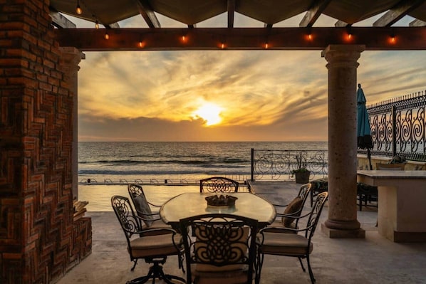 A terrace with a table and chairs, overlooking the sea at sunset.