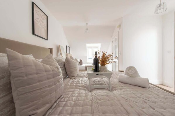 Habitación de hotel con una cama grande, una mesita de noche, un jarrón con flores secas y vista al pasillo.