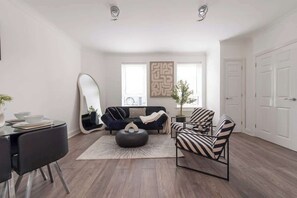 En moderne stue med sofa, lænestole, spisebord og et stort spejl.