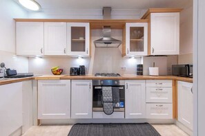 A modern kitchen with white cabinets, a gas stove, a microwave, and a kettle.