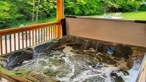 A hot tub on a wooden deck with a view of a green landscape. - S'more Adventure - NEW! Red River Gorge Creekside Cabin 2 Bedroom with Hot Tub (Campton)