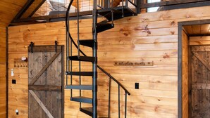 A spiral staircase in a wooden interior with a lofted ceiling and a large wooden door. - S'more Adventure - NEW! Red River Gorge Creekside Cabin 2 Bedroom with Hot Tub (Campton)
