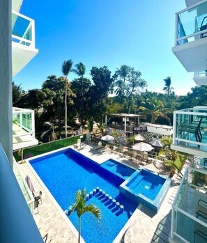 A swimming pool with a clear blue water feature, surrounded by lounge chairs and umbrellas, set against a backdrop of palm trees and a clear sky. - Gran Palma (Acapulco)