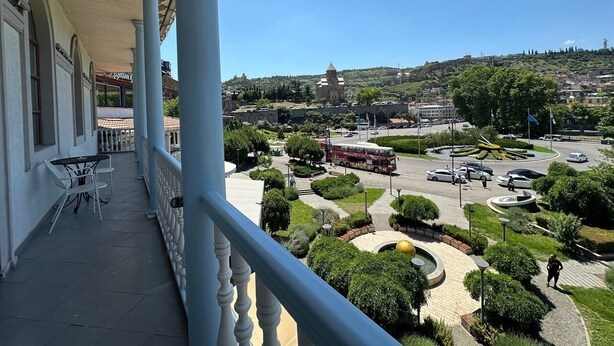 A balcony with a view of a cityscape, including a roundabout and a hill with buildings. - hotel europe meidan (Tbilisi)