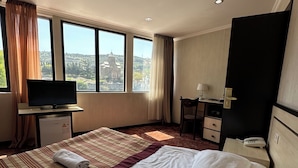 A hotel room with a large bed, a desk, a television, and a view of a cityscape. - hotel europe meidan (Tbilisi)