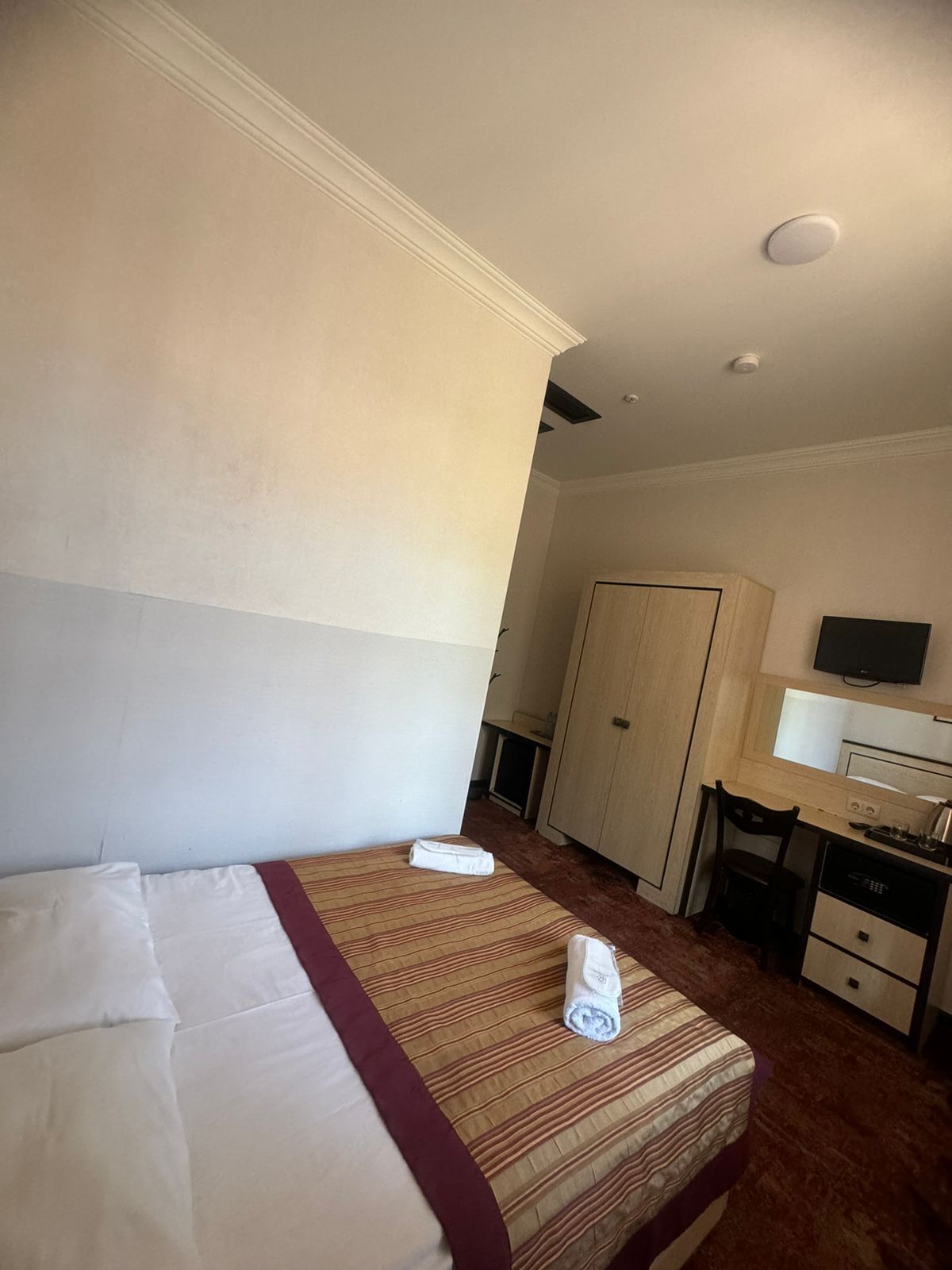 A hotel room with a bed, a desk, a television, and a wardrobe.