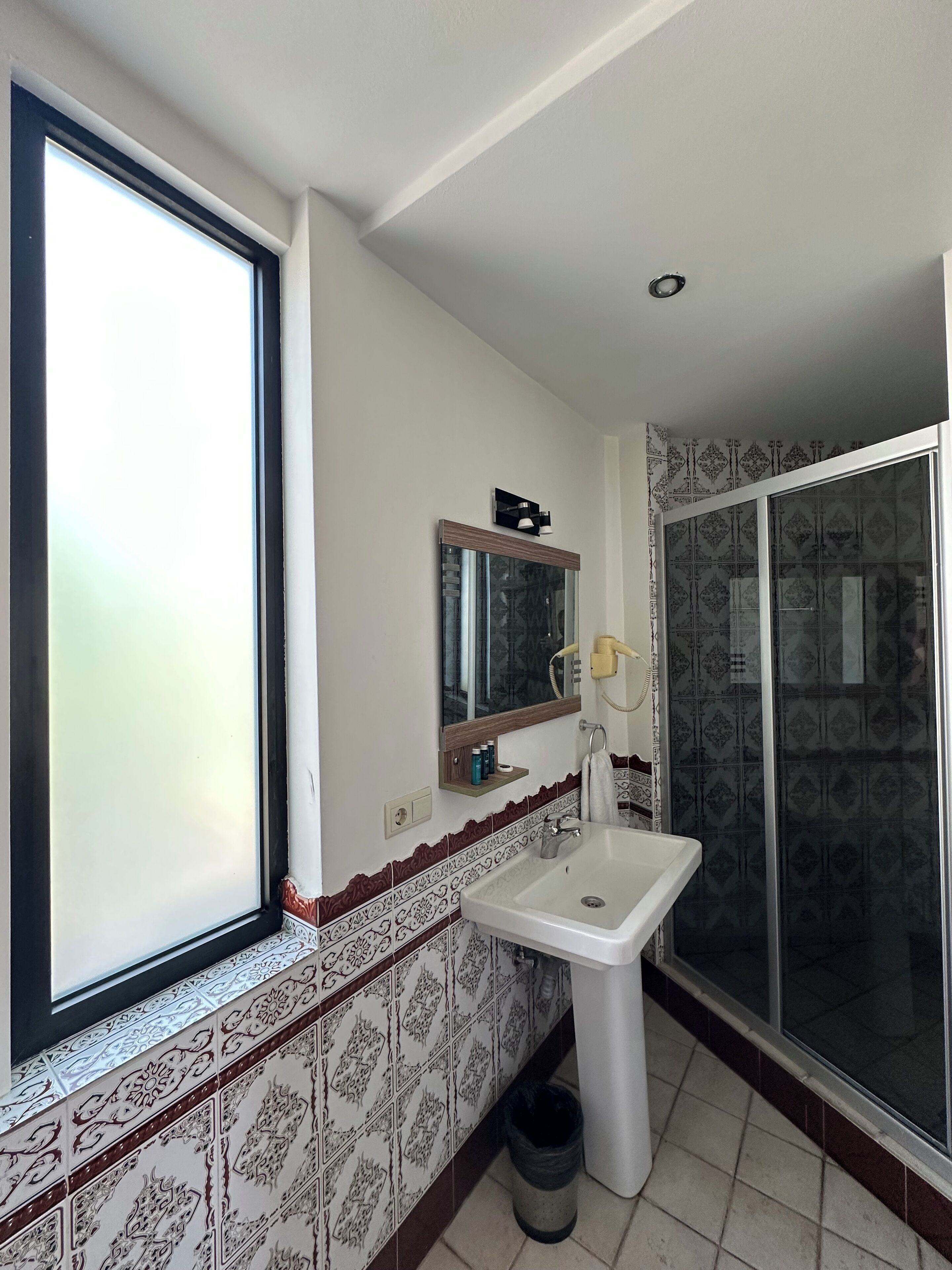 A bathroom with a large window, a sink, a mirror, and a shower area.