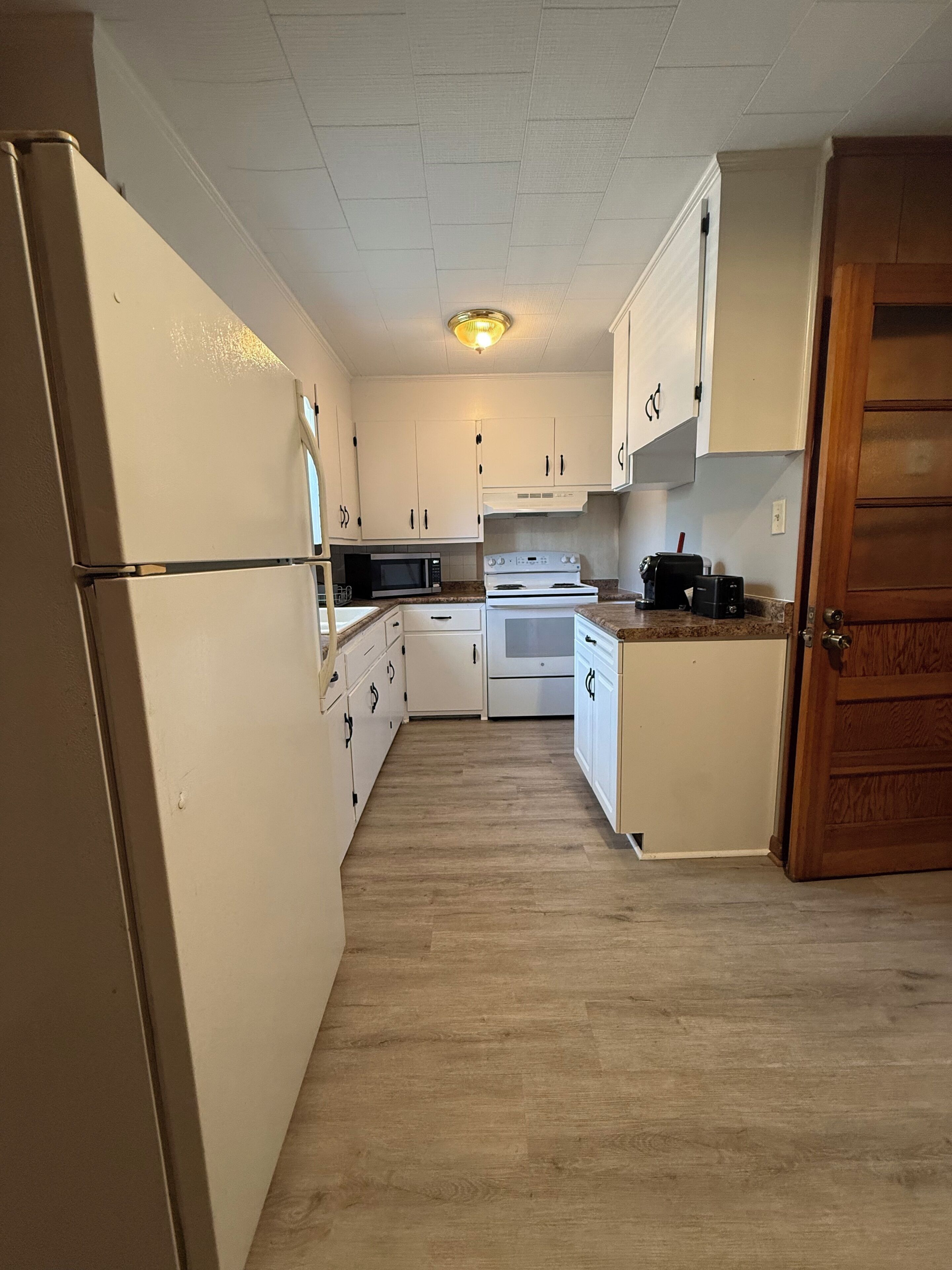 A kitchen with white cabinets, a microwave, an oven, and a refrigerator.