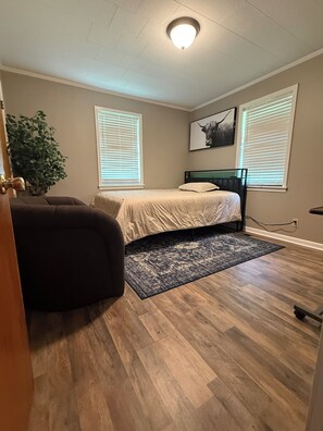 A bedroom with a bed, a dark armchair, a potted plant, and a ceiling light fixture.