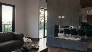 A modern living room with a leather sofa, a dining area with black chairs, and a kitchen with a large island. - Emerald Toucan Estate - 5 BR Mountain Retreat in Nature (San Bosco de Santa Barbara)