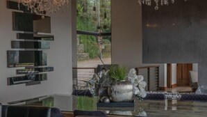 A modern dining area with a glass table, dark chairs, a chandelier, and a view of greenery outside. - Emerald Toucan Estate - 5 BR Mountain Retreat in Nature (San Bosco de Santa Barbara)