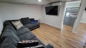 Ein Wohnzimmer mit einer Eckcouch, einem an der Wand montierten Flachbildfernseher und Holzboden.
