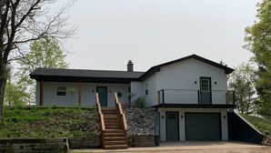 Ein zweigeschossiges Haus mit Auffahrt, einer Holztreppe und einer Steinmauer.