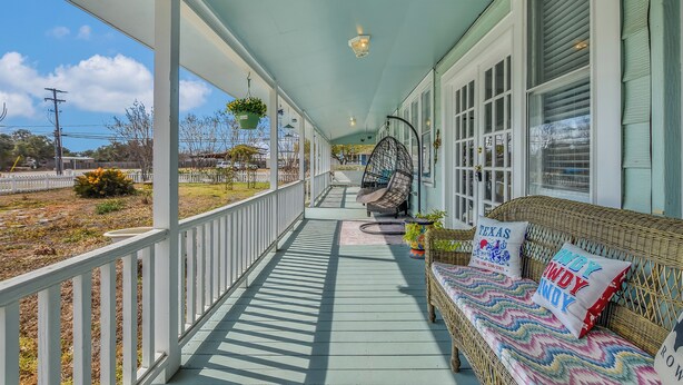A covered porch with a wicker sofa, hanging plants, and a view of the yard.