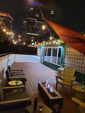 Terraza en la azotea con mobiliario exterior, una chimenea y luces colgantes.