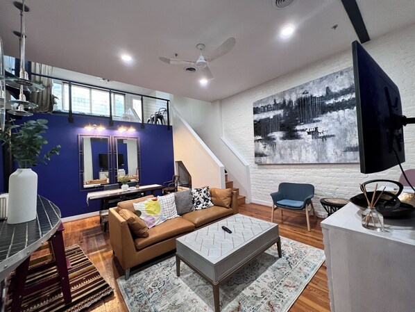 Una sala de estar moderna con una pared azul de acento, un cuadro grande, un sofá, una mesa de centro y una escalera que sube a un nivel superior.