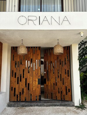 Ein Gebäudeeingang, über den die Schriftzug „ORIANA“ prangt. Zwei hängende Korblampen befinden sich über dem Eingang.