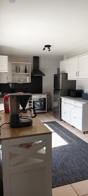A modern kitchen with white cabinets, a black range hood, a coffee maker, an oven, and a microwave. - Family home in Pleumeur-Bodou in the heart of the Pink Granite Coast (Pleumeur-Bodou)