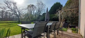 Eine Terrasse im Freien mit Tisch und Stühlen, umgeben von Pflanzen und Bäumen.