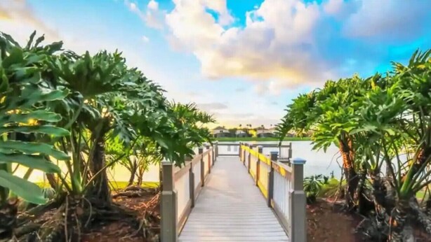 A wooden pathway leading to a body of water, flanked by lush greenery and a clear sky. - Comfortable Home at Berkley Resort (Kissimmee)