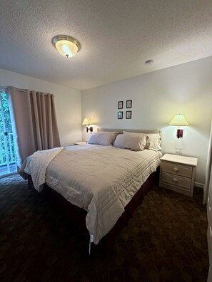 A bedroom with a bed, two bedside tables with lamps, a window with curtains, and a ceiling light. - Comfortable Home at Berkley Resort (Kissimmee)