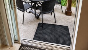 A glass door leading to an outdoor patio with a round table and four chairs, surrounded by lush greenery. - Comfortable Home at Berkley Resort (Kissimmee)