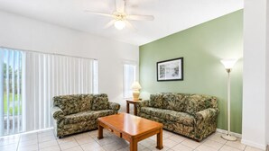 A living room with two patterned sofas, a wooden coffee table, a floor lamp, and a ceiling fan. - The Ideal Getaway V | 3BR near Disney & Pool (Kissimmee)