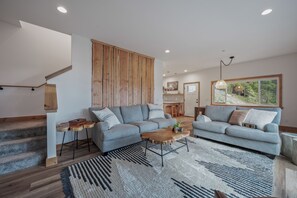 A modern living room with a grey sofa, wooden coffee table, and a staircase with wooden railings. - Unplug in Nature + Cabin in the Pines + Hot Tub, Game Room, Near the Lake (Ronald)