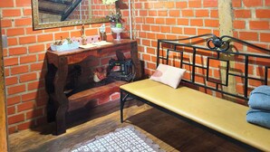 Une pièce mansardée chaleureuse avec des poutres apparentes, un mur de briques, un banc en bois, une machine à coudre et un ventilateur.