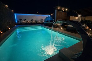 Piscina com cachoeira artificial, cercada por um muro de pedra e plantas em vasos.