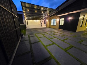 Uma área externa coberta com piso de pedra e grama sintética, teto de metal e iluminação externa.