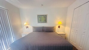 Une chambre avec un grand lit, deux lampes de chevet, une œuvre d’art encadrée au-dessus du lit et une armoire sur le côté droit.