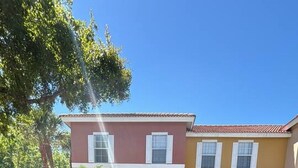 Un bâtiment à deux étages, doté d’une façade rouge et jaune, d’un parking et d’arbres qui projettent des ombres.