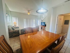 A dining area with a wooden table and chairs, a sofa, and a television in the background. - Your next adventure 3 (Kissimmee)