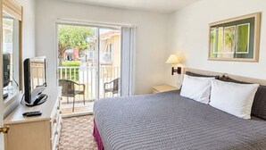 Een hotelkamer met een bed, een bureau met een computer, een stoel en uitzicht op het exterieur.