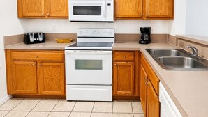 Une cuisine avec des meubles de rangement en bois, un four à micro-ondes, une cuisinière, une machine à café et un évier.