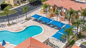 Une piscine entourée de chaises longues et de parasols, avec un bâtiment en arrière-plan.